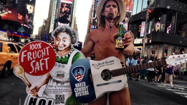 Der „Naked Cowboy“ mit Gitarre und einer Tafel „100% Fruchtsaft“ am Times Square in New York.