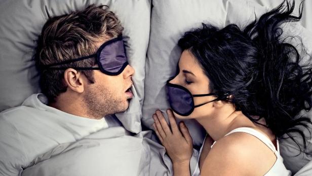 Ein Paar schläft mit Schlafmasken im Bett.