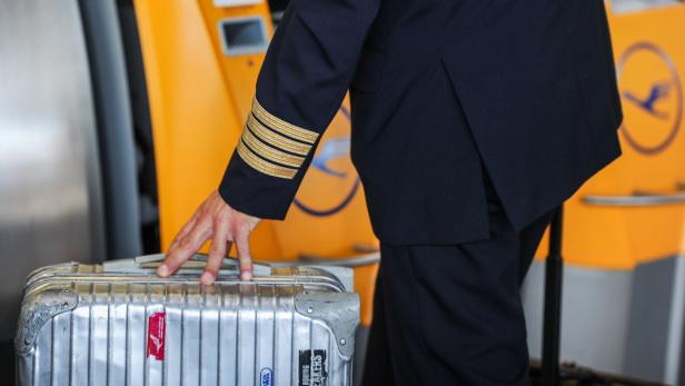 Ein Pilot der Lufthansa mit seinem Koffer vor einem Check-in-Schalter.