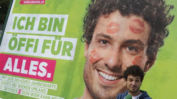 Ein Mann steht vor einem Wahlplakat der Grünen mit dem Slogan „Ich bin Öffi für alles“.