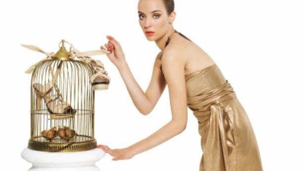 Eine Frau im goldenen Kleid betrachtet Schuhe in einem goldenen Vogelkäfig.