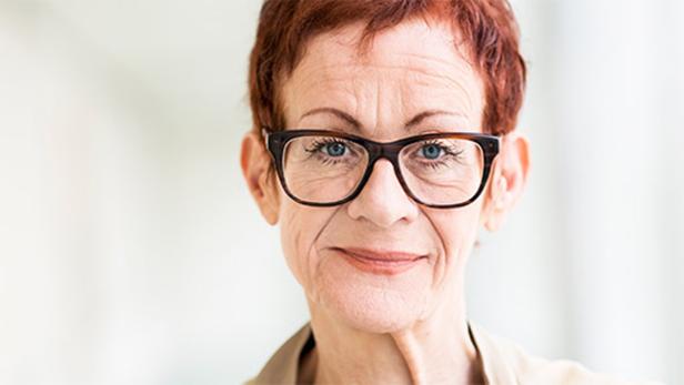 Eine Frau mit kurzen roten Haaren und Brille blickt in die Kamera.