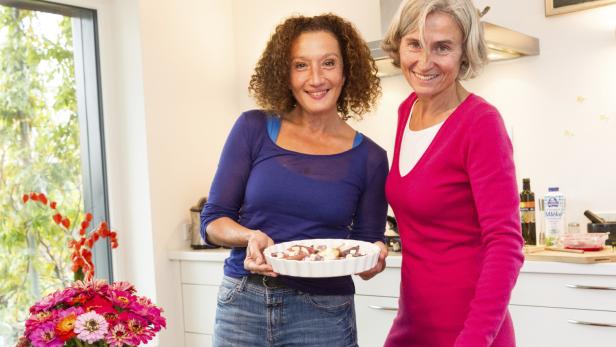 Zwei Frauen stehen lächelnd in einer Küche, eine hält eine Quiche.