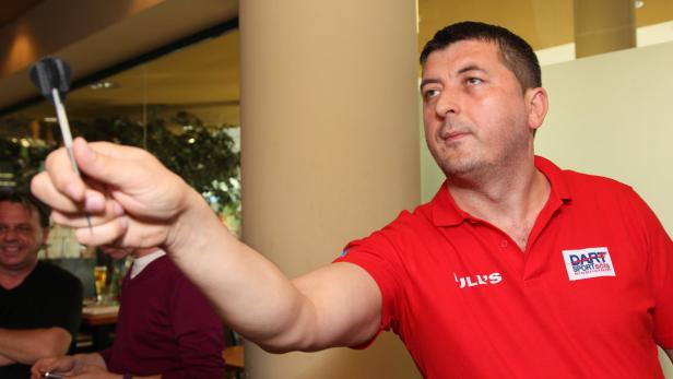 Ein Mann im roten Poloshirt zielt mit einem Dartpfeil.