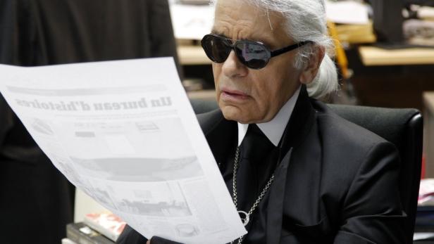 Karl Lagerfeld liest eine Zeitung mit dunkler Sonnenbrille.
