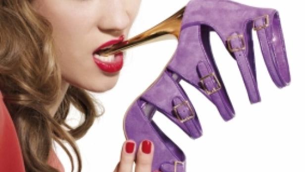 Eine Frau hält einen lila High Heel im Mund.