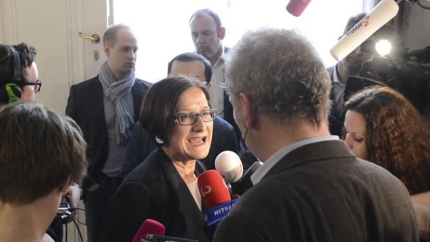 Eine Frau mit Brille wird von mehreren Reportern interviewt.