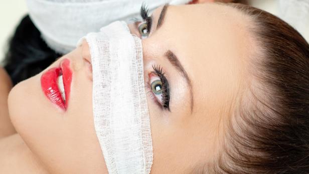 Eine Frau liegt mit einem Verband um die Nase und roten Lippenstift auf den Lippen.