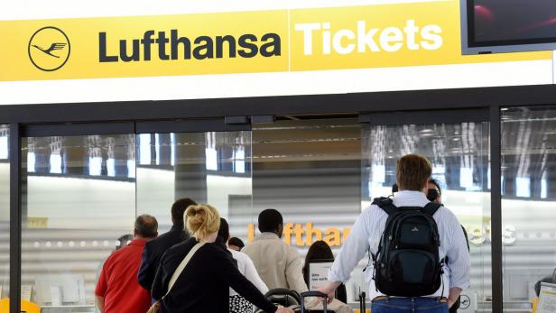 Menschen stehen vor einem Lufthansa Ticketschalter an einem Flughafen an.