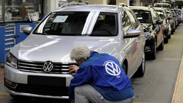Ein Arbeiter in Arbeitskleidung inspiziert einen silbernen Volkswagen in einer Fabrikhalle.