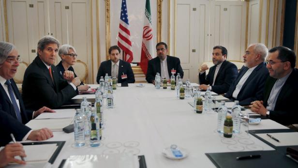 Delegationen der USA und des Iran sitzen an einem Tisch mit den jeweiligen Nationalflaggen im Hintergrund.