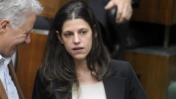 Eine Frau mit dunklen Haaren und dunklem Blazer steht neben einem älteren Mann.