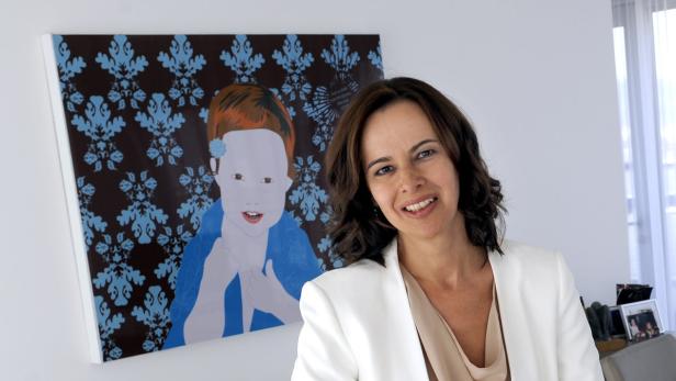 Eine Frau lächelt vor einem Gemälde mit einem Kind darauf.