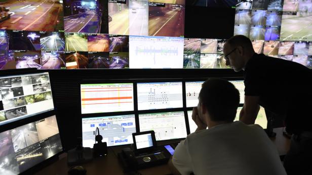 Zwei Männer arbeiten in einer Verkehrsleitzentrale vor mehreren Monitoren, die Überwachungskamera-Aufnahmen zeigen.