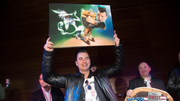Ein Mann hält ein Bild mit einer Karikatur von sich selbst mit Ziehharmonika und einem Drachen hoch.