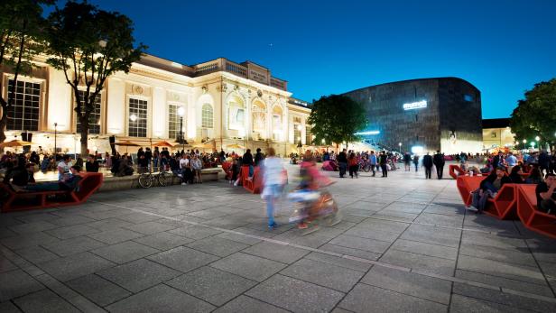 Am Abend sitzen Menschen vor dem Museumsquartier in Wien.