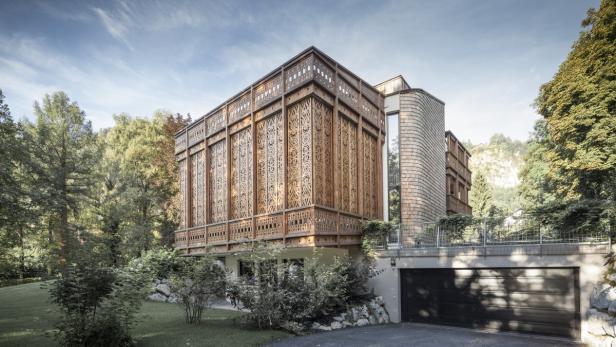Ein modernes Haus mit Holzfassade und aufwendigen Schnitzereien, umgeben von Bäumen.