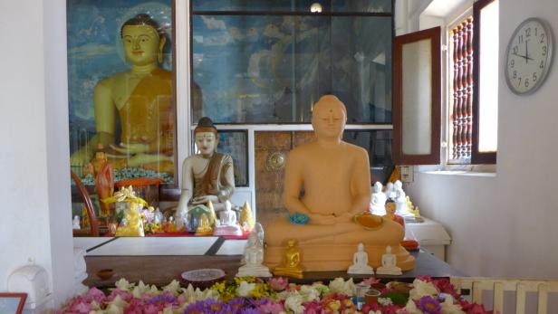 Mehrere Buddha-Statuen stehen auf einem Tisch mit Blumen.