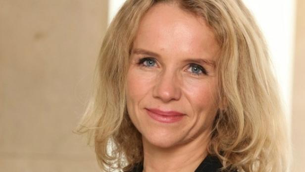 Porträt einer Frau mit blonden, gewellten Haaren und blauen Augen.