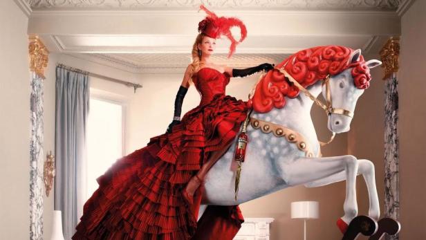 Eine Frau in einem roten Kleid reitet auf einem weißen Spielzeugpferd mit roter Mähne.