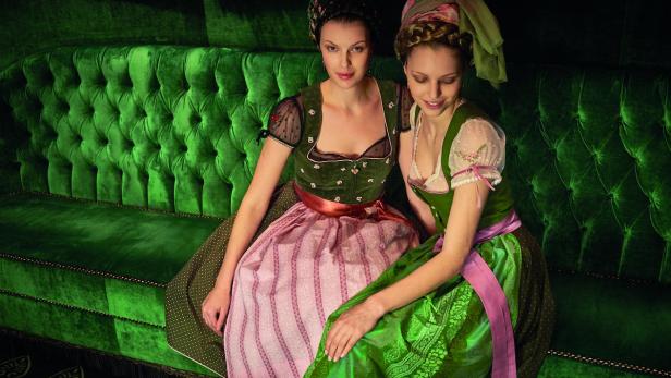 Zwei Frauen in Dirndln sitzen auf einem smaragdgrünen Sofa.