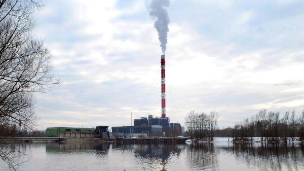 Ein Heizkraftwerk mit einem rot-weiß gestreiften Schornstein spiegelt sich im Wasser.