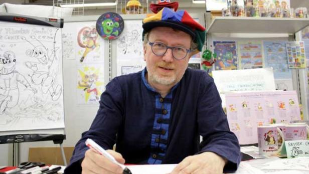 Ein Mann mit einer bunten Mütze zeichnet eine Comicfigur.