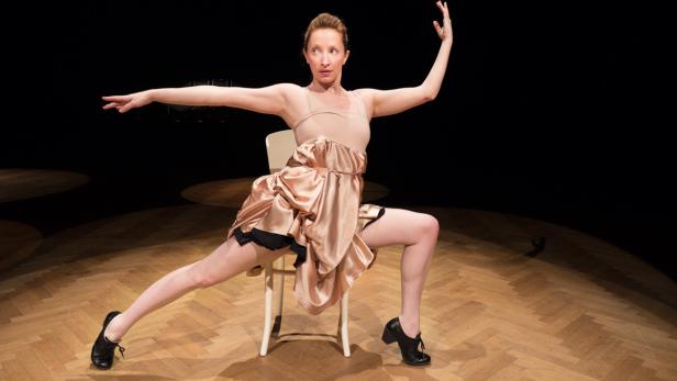 Eine Frau in einem Kleid sitzt auf einem Stuhl und posiert auf einer Bühne.