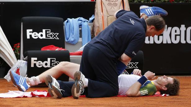 Ein Tennisspieler liegt verletzt auf dem Platz, während ein Betreuer sich um ihn kümmert.