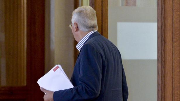 Ein Mann mit Anzug und Papierstapel verlässt einen Raum.