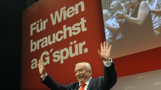 Ein Mann mit Schnurrbart steht vor einem roten Plakat mit der Aufschrift „Für Wien brauchst a G’spür“.