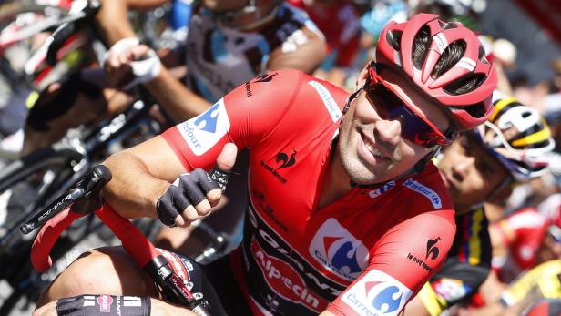 Ein Radrennfahrer im roten Trikot lächelt in die Kamera.