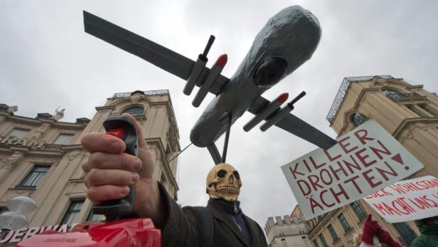 Eine Person mit Totenkopfmaske demonstriert mit einer Drohnenattrappe und einem Schild gegen „Killer Drohnen“.