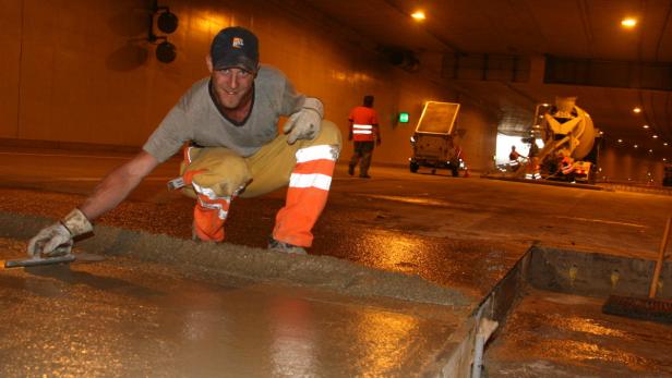 Ein Bauarbeiter glättet Beton in einem Tunnel.