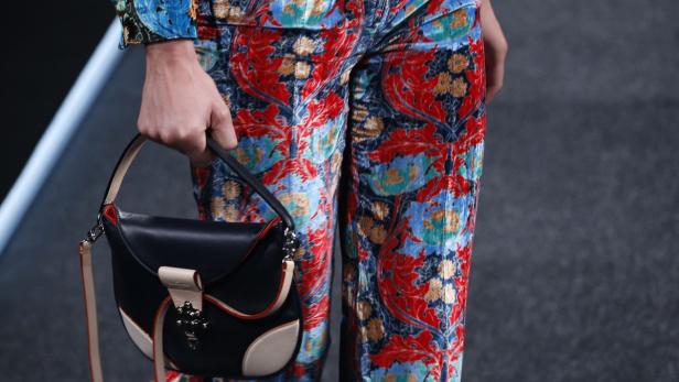 Eine Person mit gemusterter Hose hält eine schwarze Handtasche.