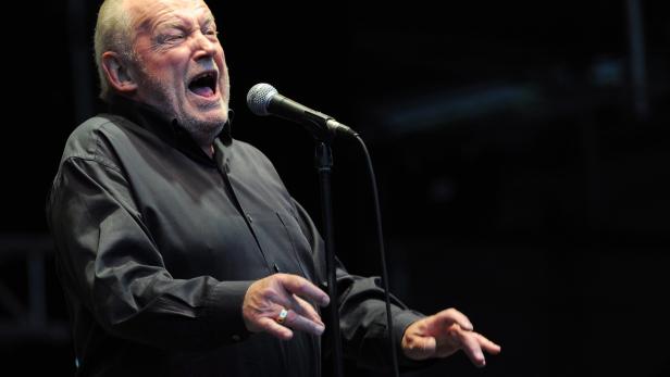 Ein älterer Mann singt mit weit geöffnetem Mund in ein Mikrofon.
