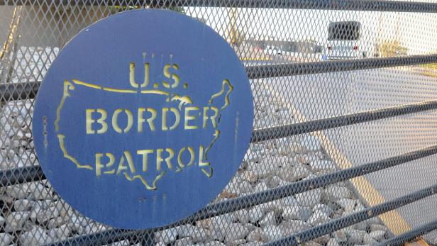 Ein Schild der U.S. Border Patrol mit einer stilisierten Karte der USA an einem Zaun.