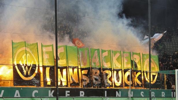 Fans von Wacker Innsbruck zünden Pyrotechnik hinter einem Banner.