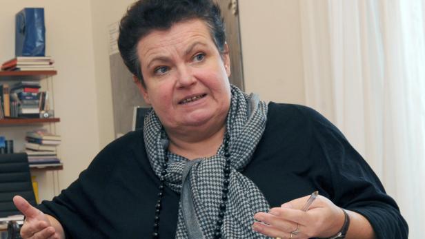 Eine Frau mit einem karierten Schal gestikuliert mit einem Stift in der Hand.