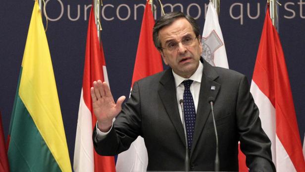 Ein Mann in einem Anzug gestikuliert vor einer Reihe von Flaggen.