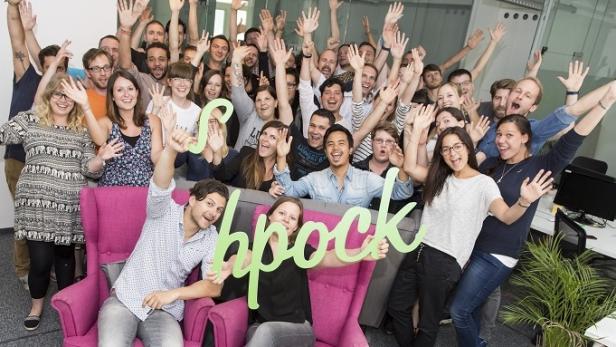 Eine große Gruppe von Menschen winkt in einem Büro in die Kamera.