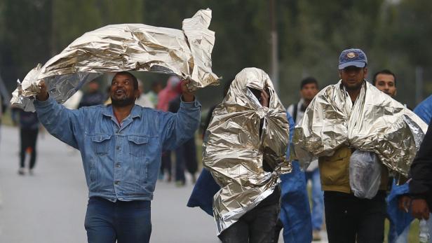 Mehrere Personen sind in Rettungsdecken gehüllt und gehen eine Straße entlang.
