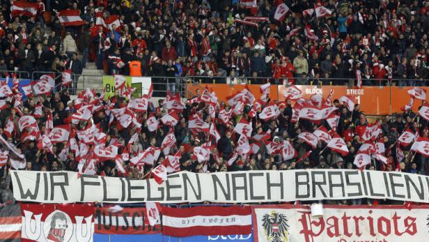 Eine Menschenmenge schwenkt rot-weiße Fahnen und hält ein Banner mit der Aufschrift „Wir fliegen nach Brasilien“.