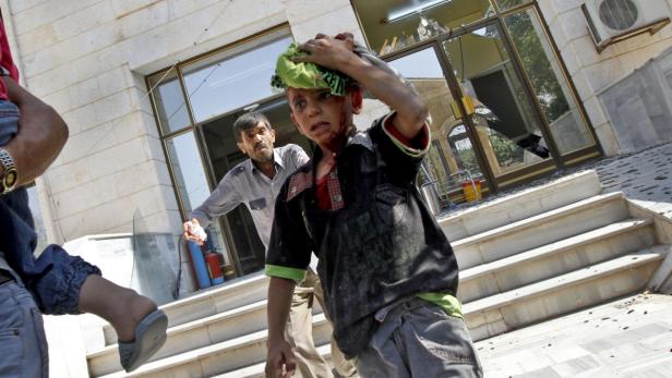 Ein verletzter Junge steht vor einem Gebäude mit zerbrochenen Fenstern.