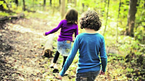 Zwei Kinder laufen einen bewaldeten Weg entlang.
