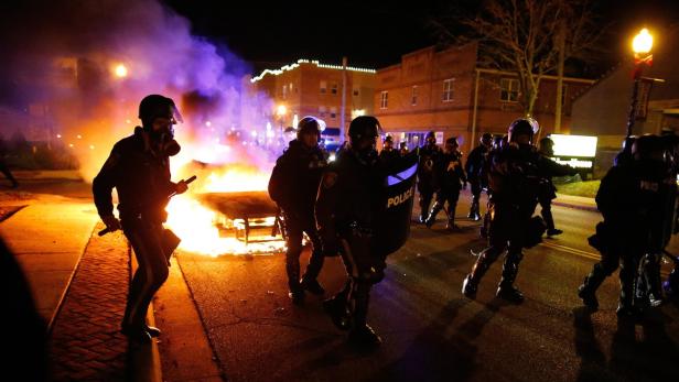 Polizisten in Schutzausrüstung stehen vor einem brennenden Barrikade auf einer Straße.
