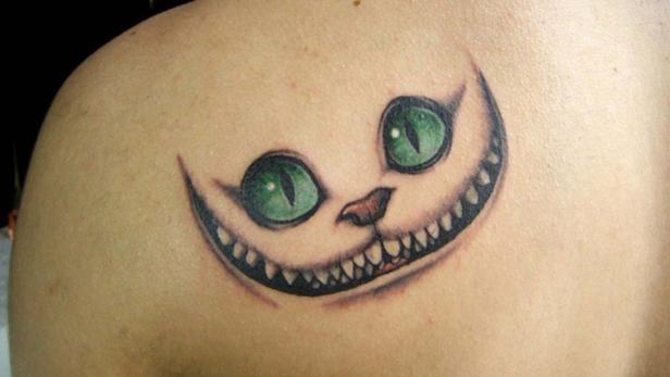 Ein Tattoo auf einer Schulter zeigt das Grinsen der Grinsekatze aus Alice im Wunderland.