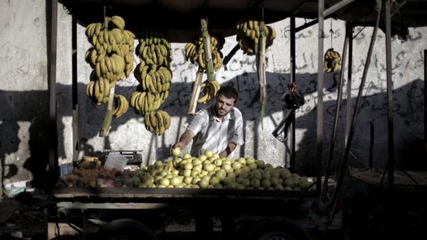 Ein Mann verkauft Bananen und Äpfel an einem Straßenstand.