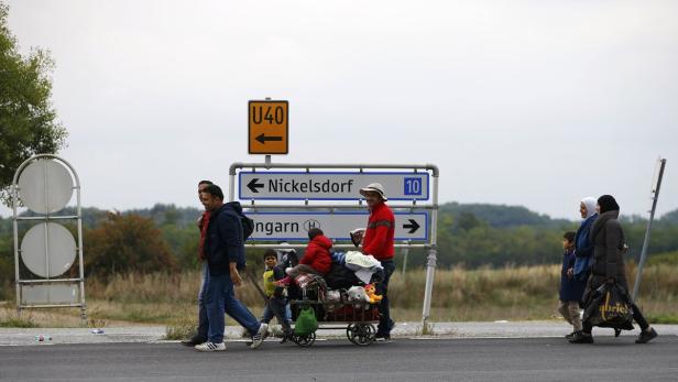 Eine Gruppe von Menschen, darunter Kinder, geht an einem Straßenschild in Richtung Nickelsdorf vorbei.