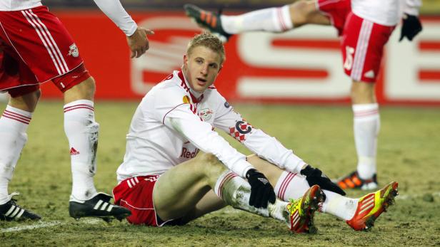 Ein Fußballspieler sitzt mit schmutzigen Stutzen auf dem Rasen.